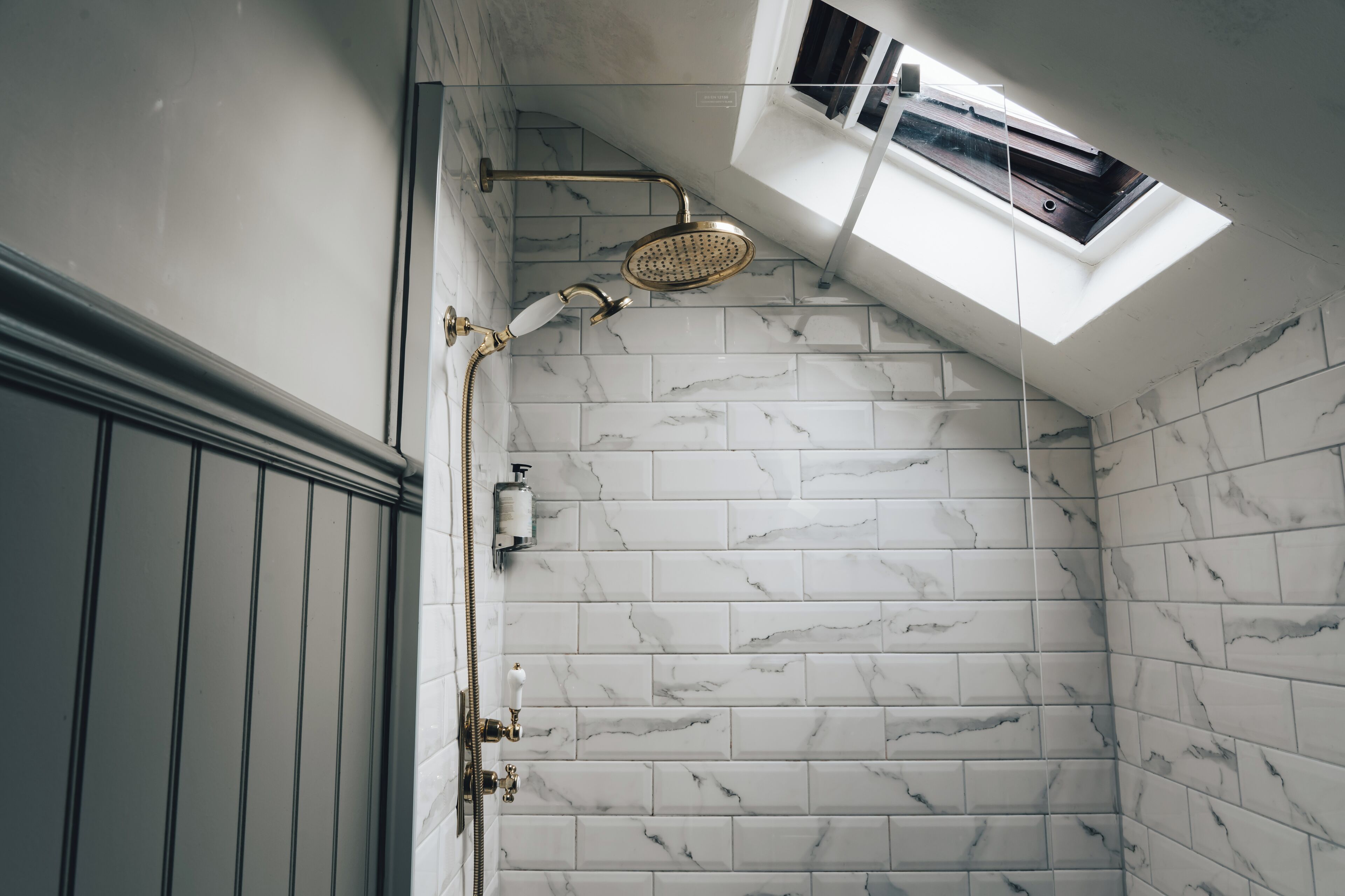 A shower with a skylight, marble tiles, and a handheld showerhead.