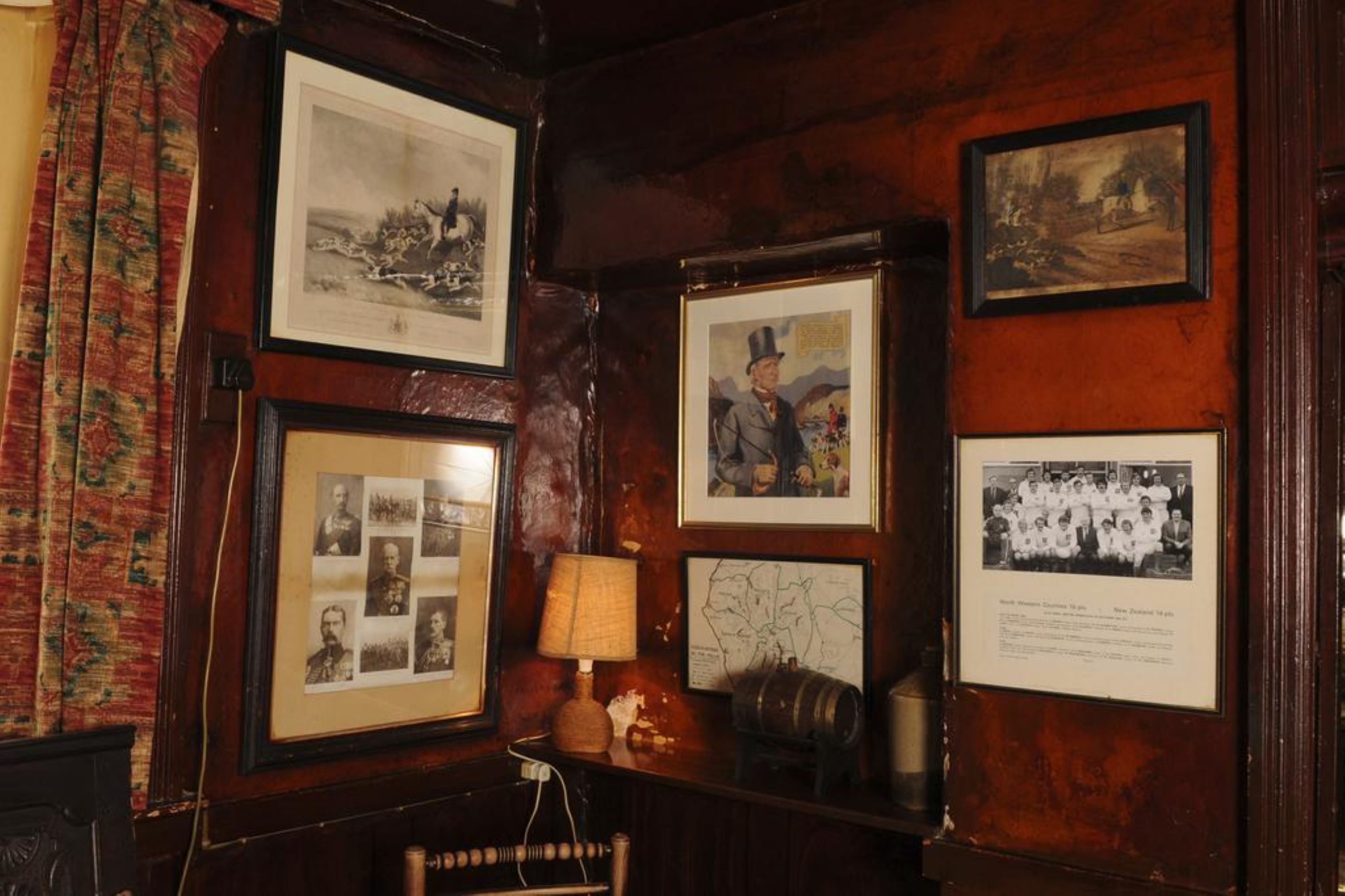 Une pièce aux murs en bois, ornée de tableaux encadrés, avec une lampe et une petite table sur laquelle est posé un objet décoratif.