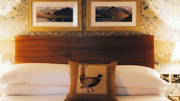 A neatly made bed with white linens, a wooden headboard, and a single decorative pillow with a bird design. Two framed pictures are hung on the wall above the bed.