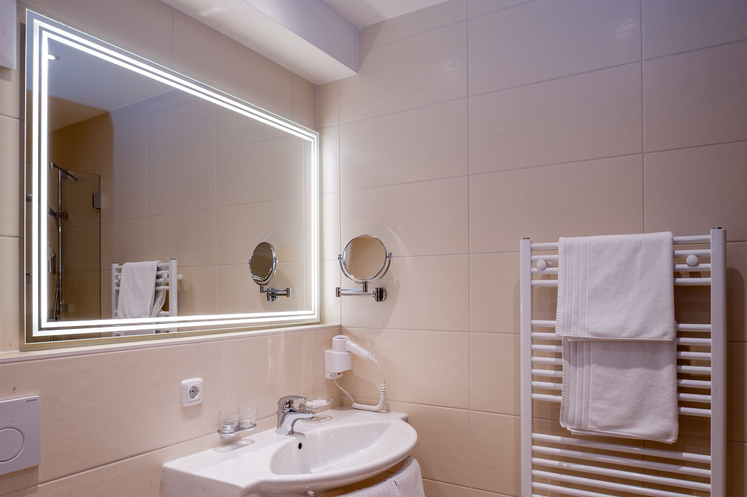 A modern bathroom with a large mirror, a sink, a towel rack, and a heated towel rail.