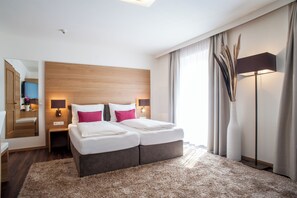 A modern hotel room with a double bed, a wooden headboard, a large mirror, a standing lamp, and a vase with decorative plants.