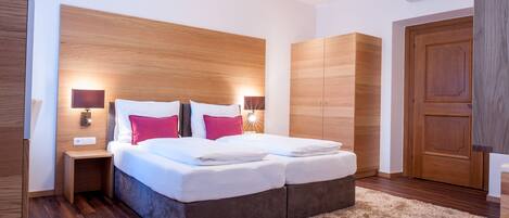 Un dormitorio moderno con cabecera de madera, cama con ropa de cama blanca y roja, dos mesitas de noche con lámparas y un armario.