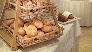 A multi-tiered wooden bread display in a banquet setting with tables and floral arrangements in the background. - Hotel Rumer Hof (Rum)