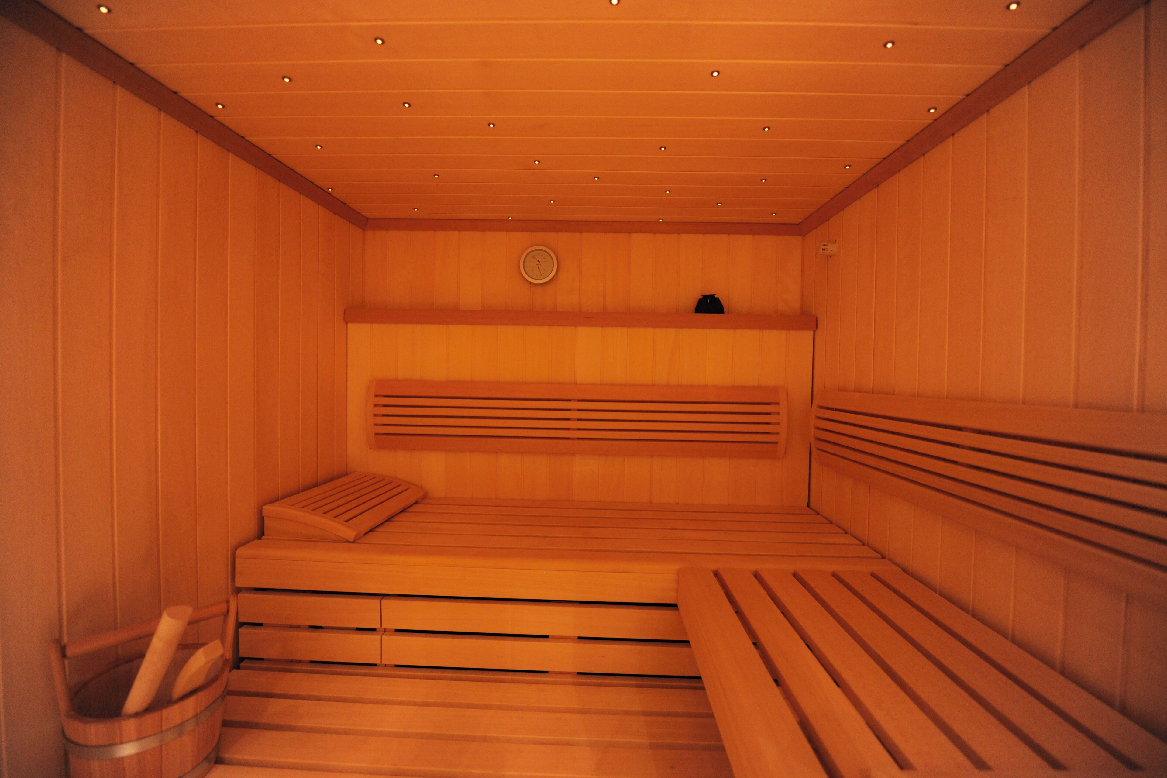 A sauna with wooden benches and a bench seat, a wooden wall, and a ceiling with recessed lighting.