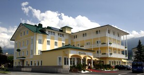 A multi-story hotel with a yellow facade, balconies, and a red carpet leading to the entrance.