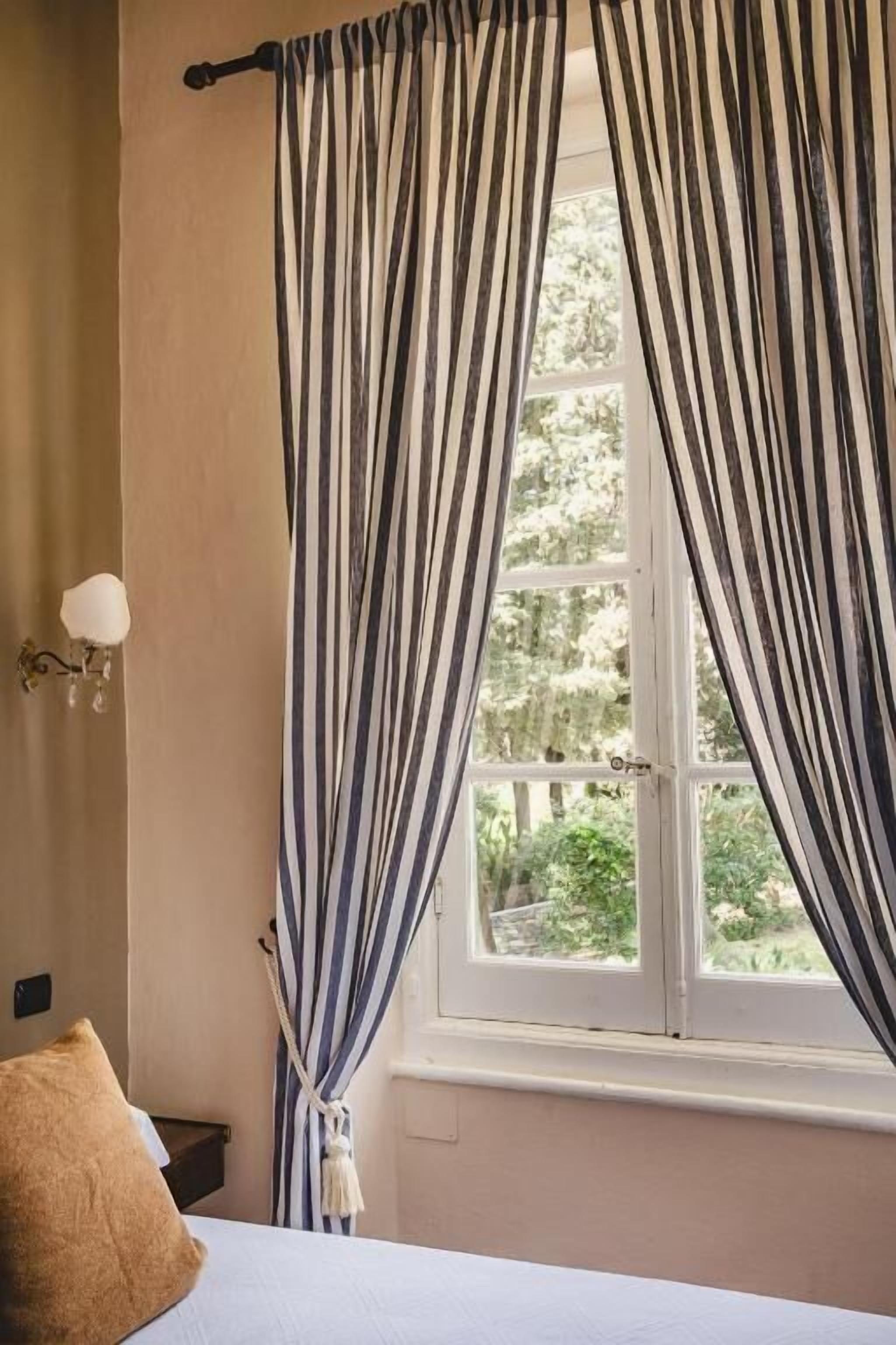 A bedroom with a bed, a window with striped curtains, and a wall-mounted light fixture.