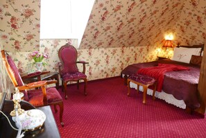 A bedroom with floral wallpaper, a red carpet, a bed with a red blanket, a wooden chair, a small table with a vase of flowers, and a nightstand with a lamp. - Rezydencja Grawert - Victorian Boutique & SPA (Ladek-Zdroj)