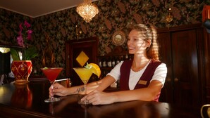 A bar area with a woman serving drinks, a decorative vase, and a patterned wallpaper background. - Rezydencja Grawert - Victorian Boutique & SPA (Ladek-Zdroj)