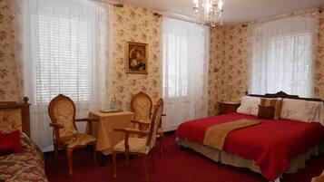 Una habitación con papel tapiz floral, una cama con ropa de cama roja, una mesa con sillas y un candelabro.
