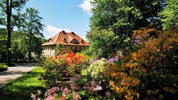 A traditional house with a sloped roof and a garden with various flowering plants. - Rezydencja Grawert - Victorian Boutique & SPA (Ladek-Zdroj)