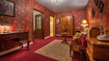 A room with a red carpet, wooden furniture, a chandelier, and floral wallpaper.
