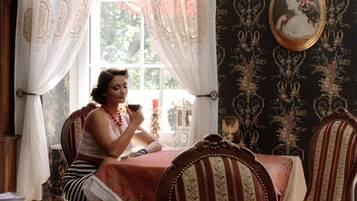 A room with a dining table, chairs, a window with curtains, a lamp, and a framed picture on the wall.