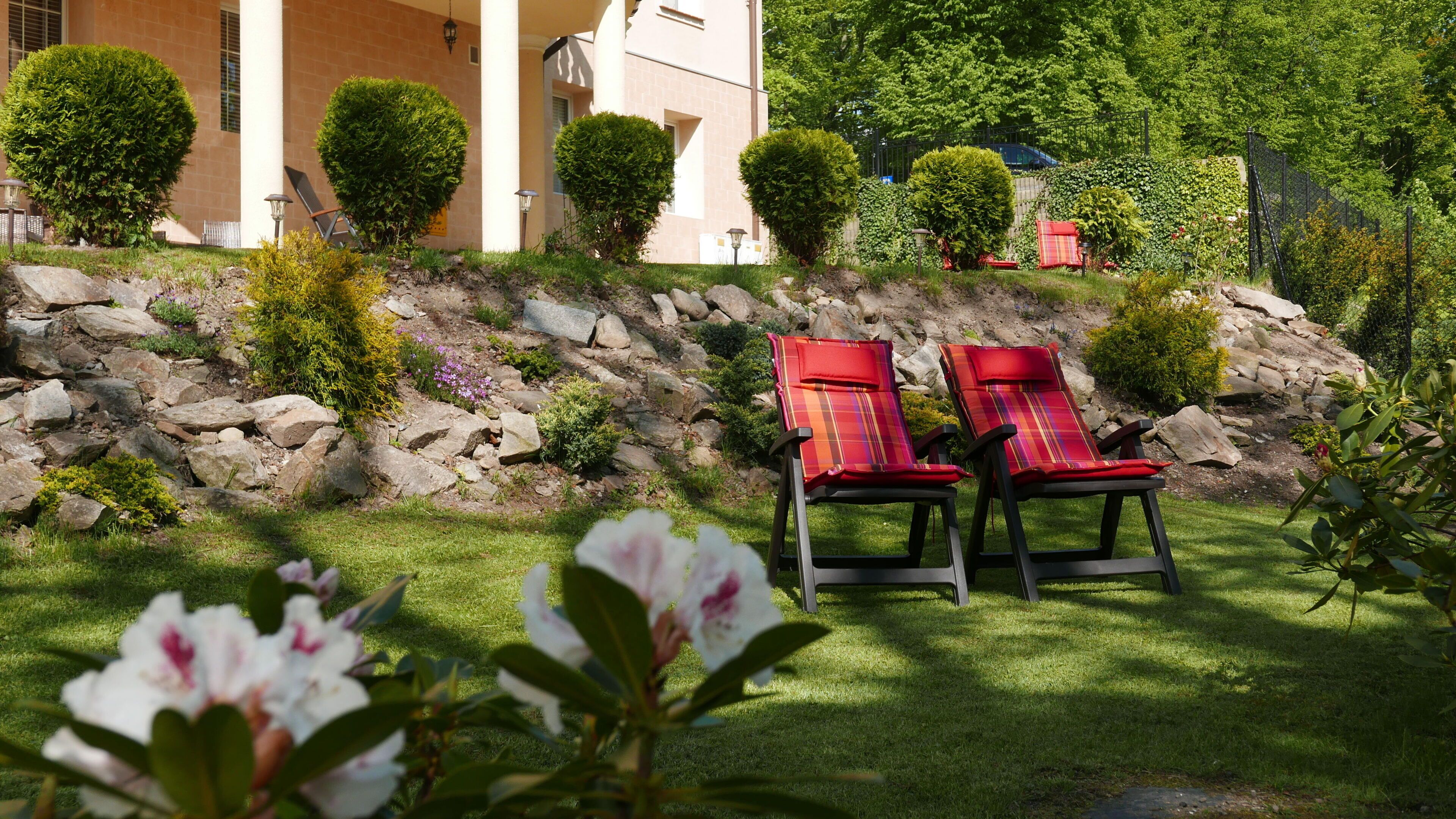 Un jardín con dos sillones rojos, un muro de piedra y un edificio al fondo.