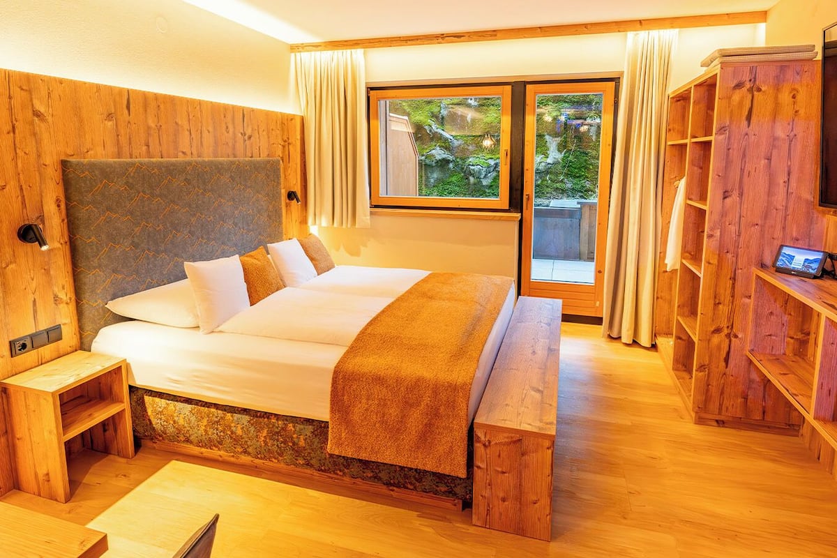 Une chambre à coucher décorée dans un style rustique, avec un lit, une télévision et une vue sur la verdure environnante.