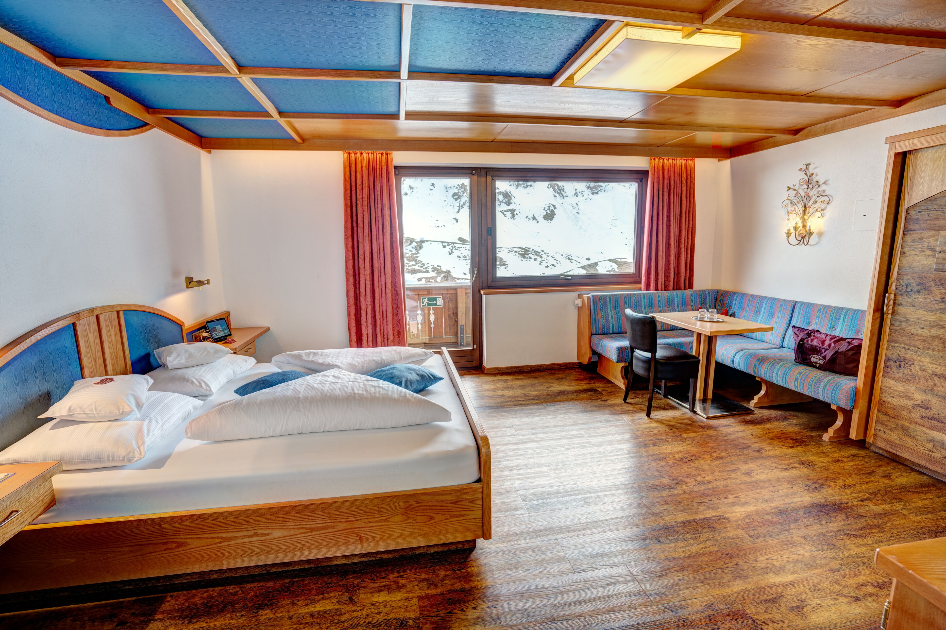 A room with a bed, a table, a bench, and a window with curtains.