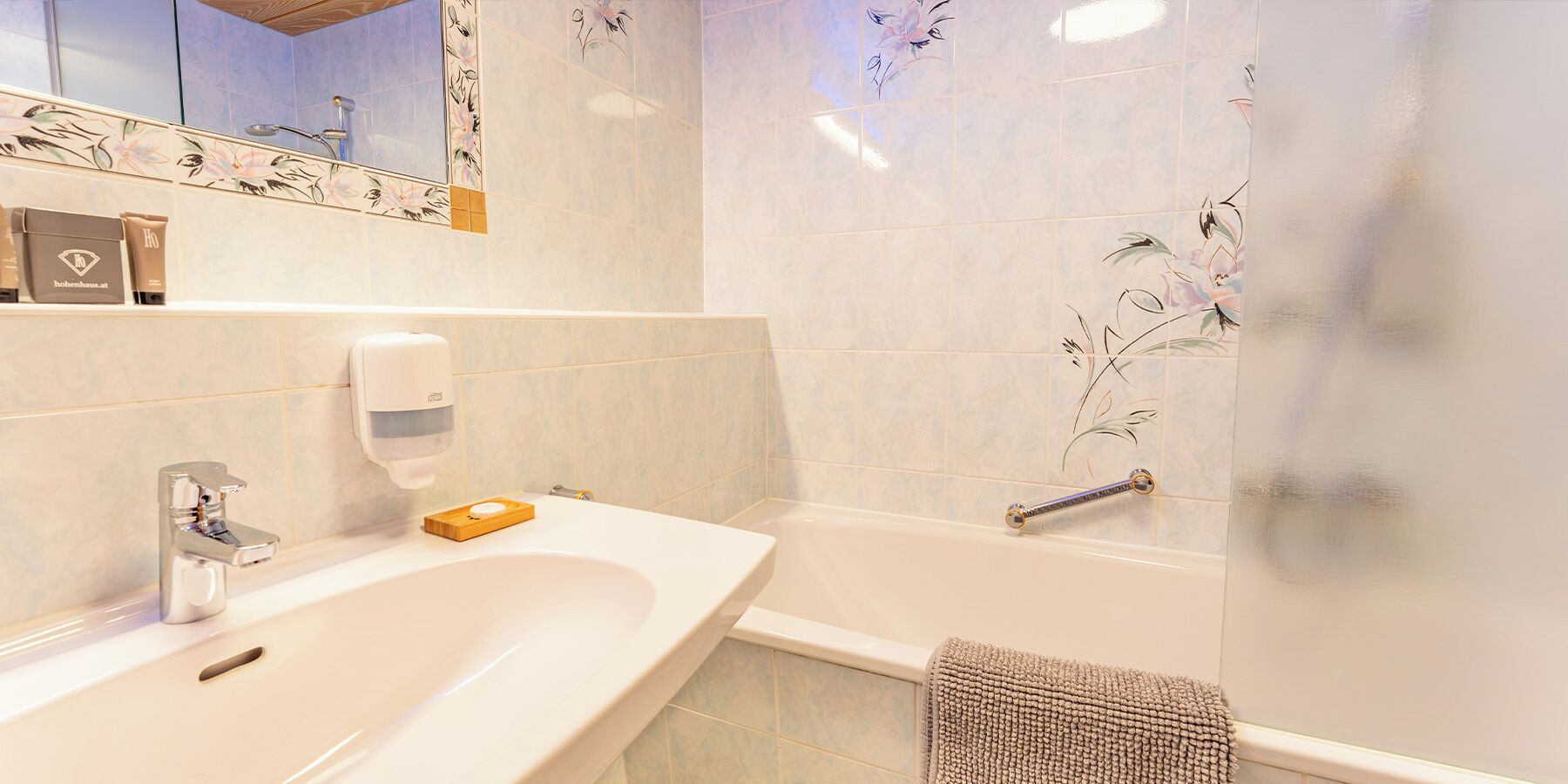 Une salle de bain équipée d’un lavabo, d’un miroir, d’un distributeur de savon liquide et d’une baignoire.
