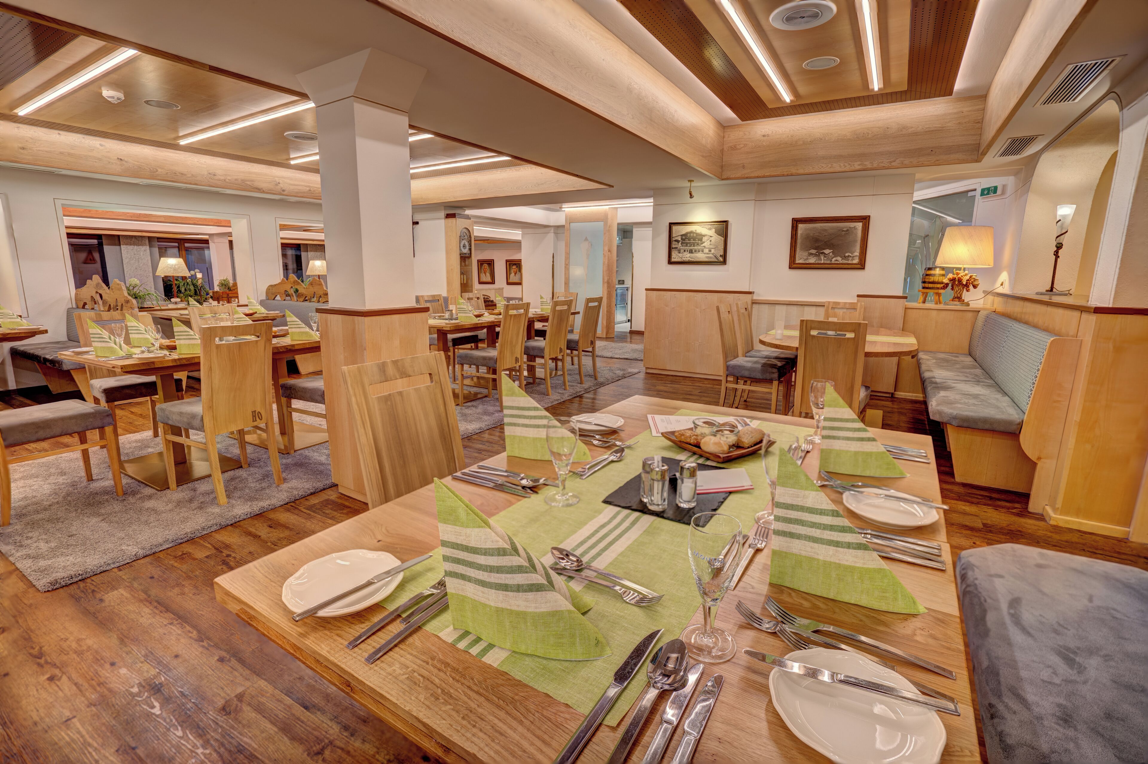 Un comedor amplio con varias mesas dispuestas para comer, sillas de madera y un diseño de techo moderno.
