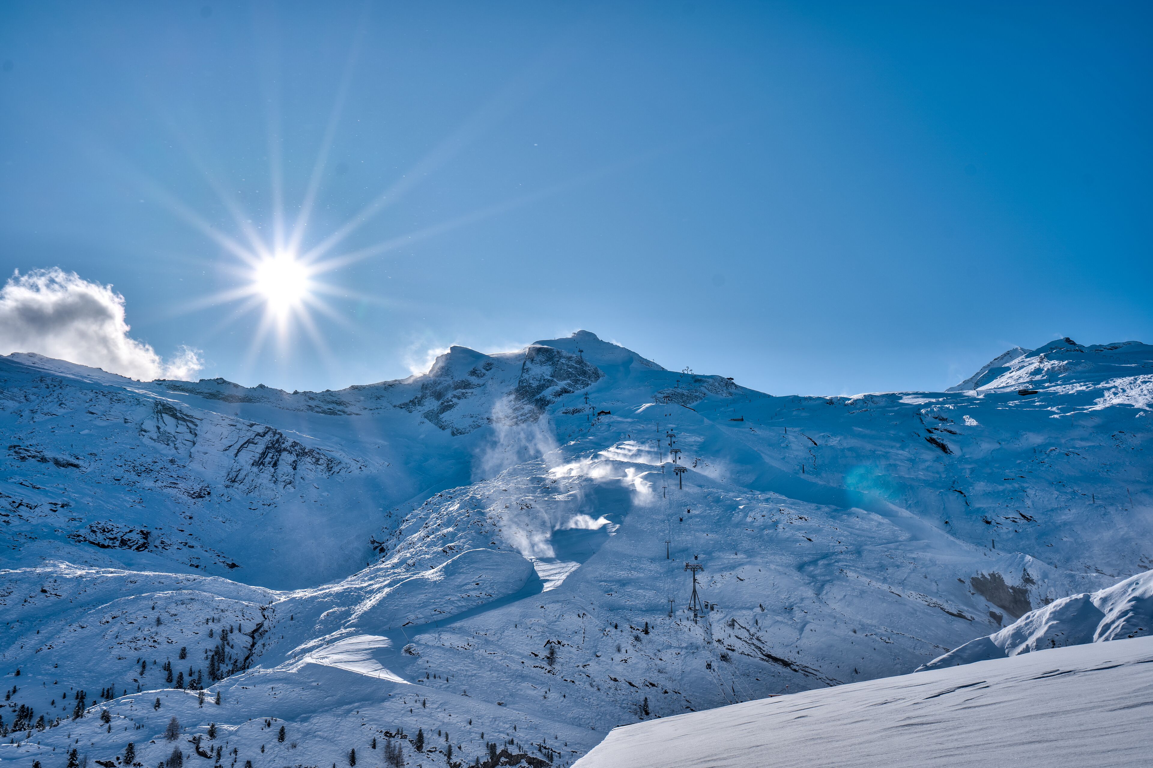 A snowy mountain landscape with clear skies and a bright sun.