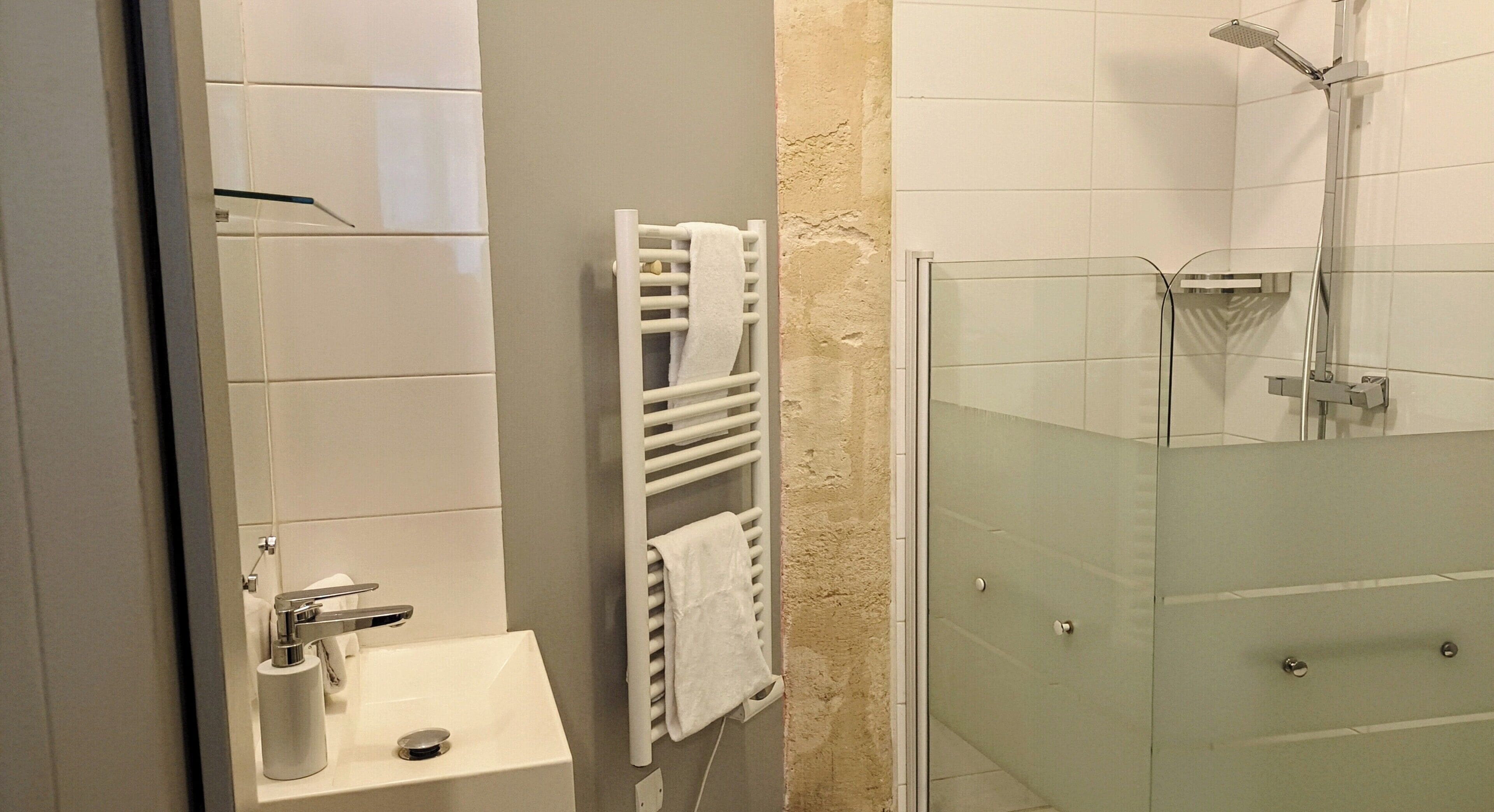 Un baño con lavamanos, toallero y cabina de ducha con mampara de vidrio.