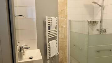 Un baño con lavamanos, toallero y cabina de ducha con mampara de vidrio.