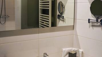Un baño moderno con un lavamanos blanco, un cabezal de ducha de mano, un perchero y un espejo.