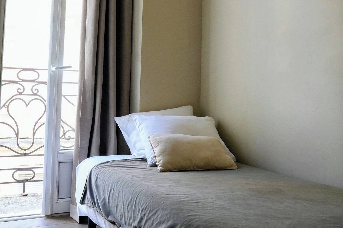 Une chambre à coucher avec un lit, une fenêtre avec des rideaux et un balcon doté d’une balustrade.