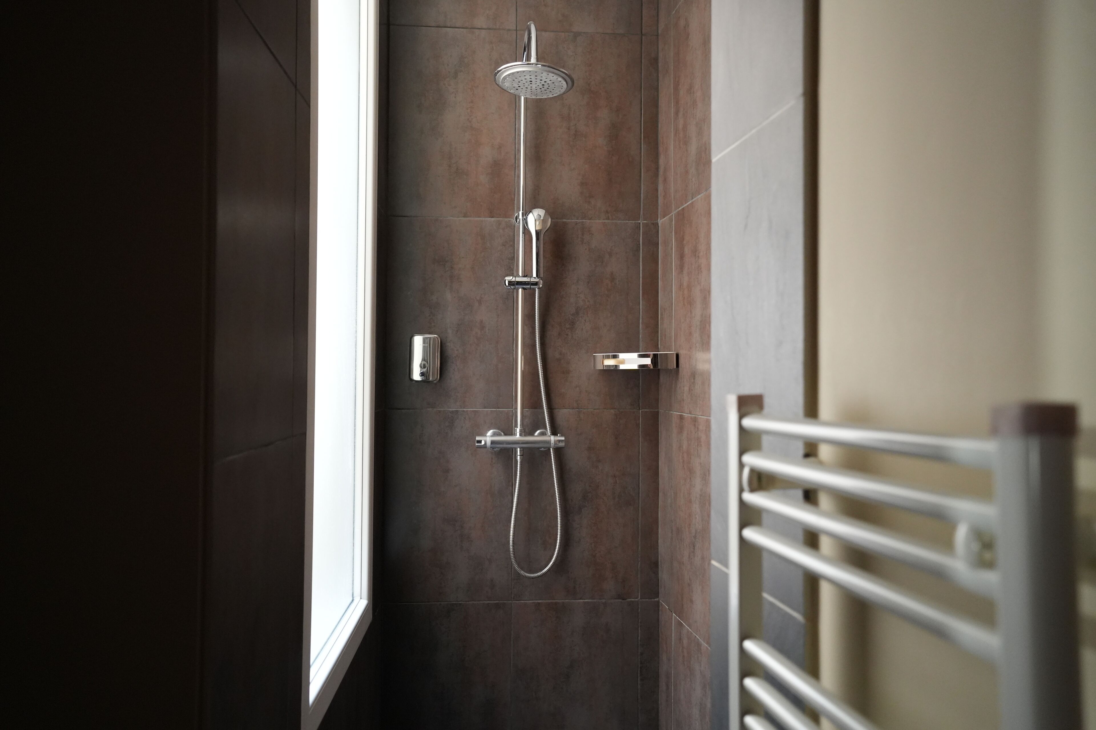 A modern shower with a handheld showerhead and a handheld hose.