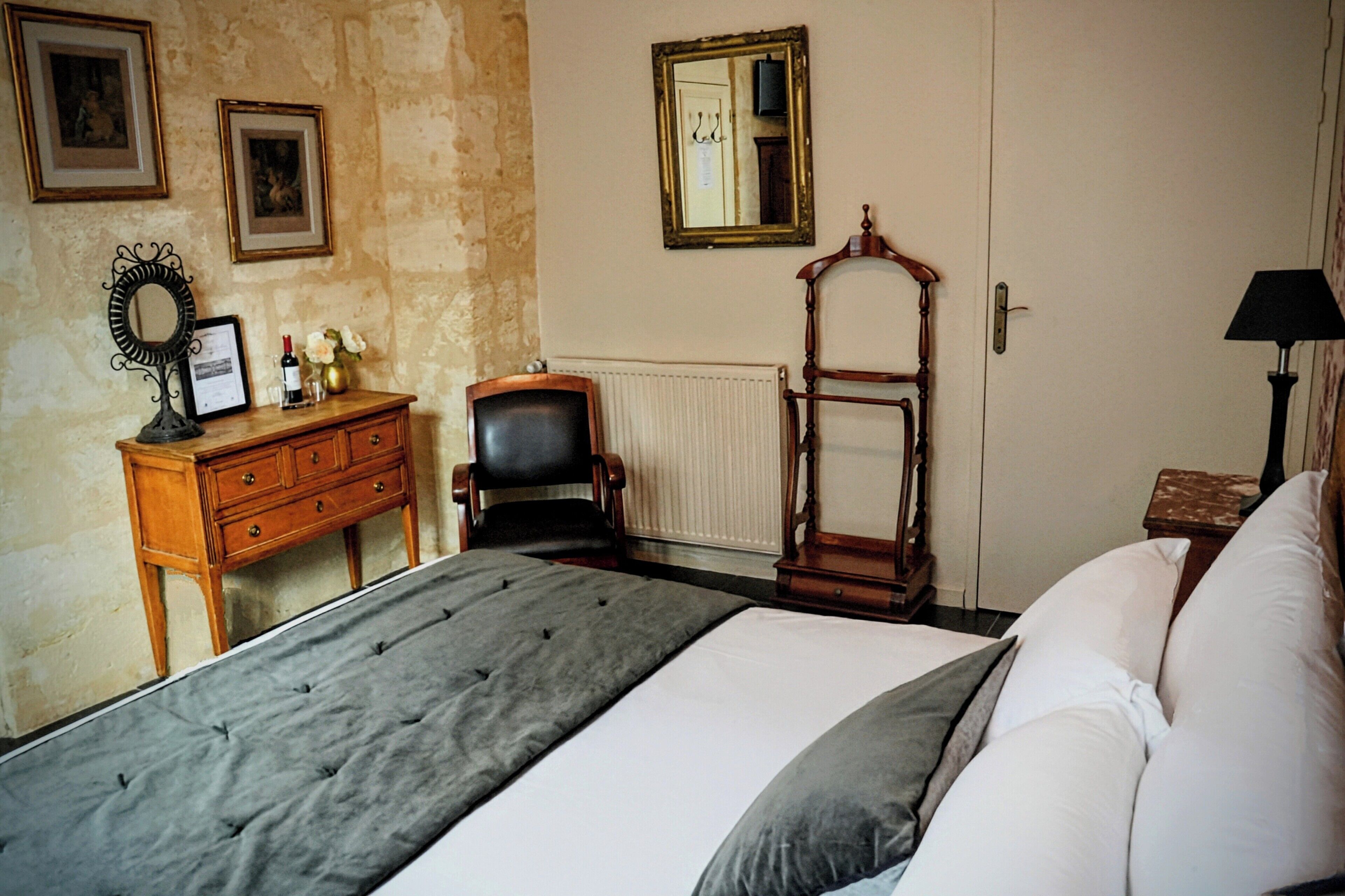 A bedroom with a large bed, a wooden dresser, a chair, a mirror, and a lamp.