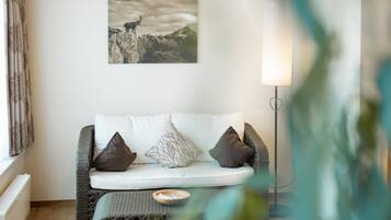 Een moderne woonkamer met een witte bank, twee zwarte kussens, een aan de muur hangend beeld van een berglandschap en een vloerlamp.