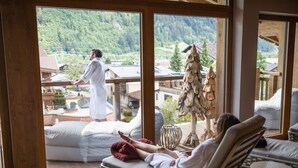 A room with a large window overlooking a mountainous area, a sofa, and a chair. - Wöscherhof (Uderns)
