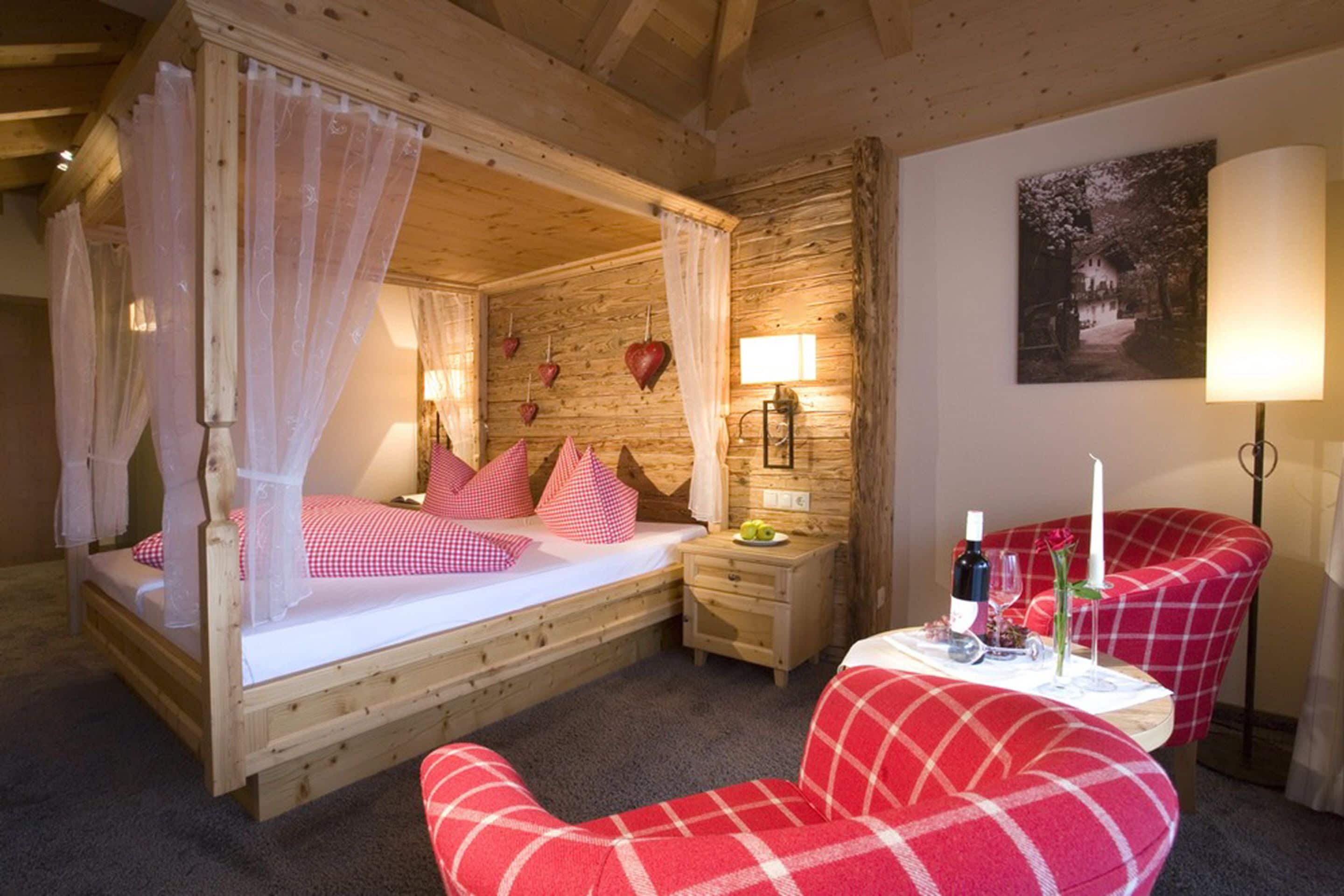 Un dormitorio acogedor con una cama de madera con dosel, una mesita de noche con lámpara y un sillón rojo a cuadros.