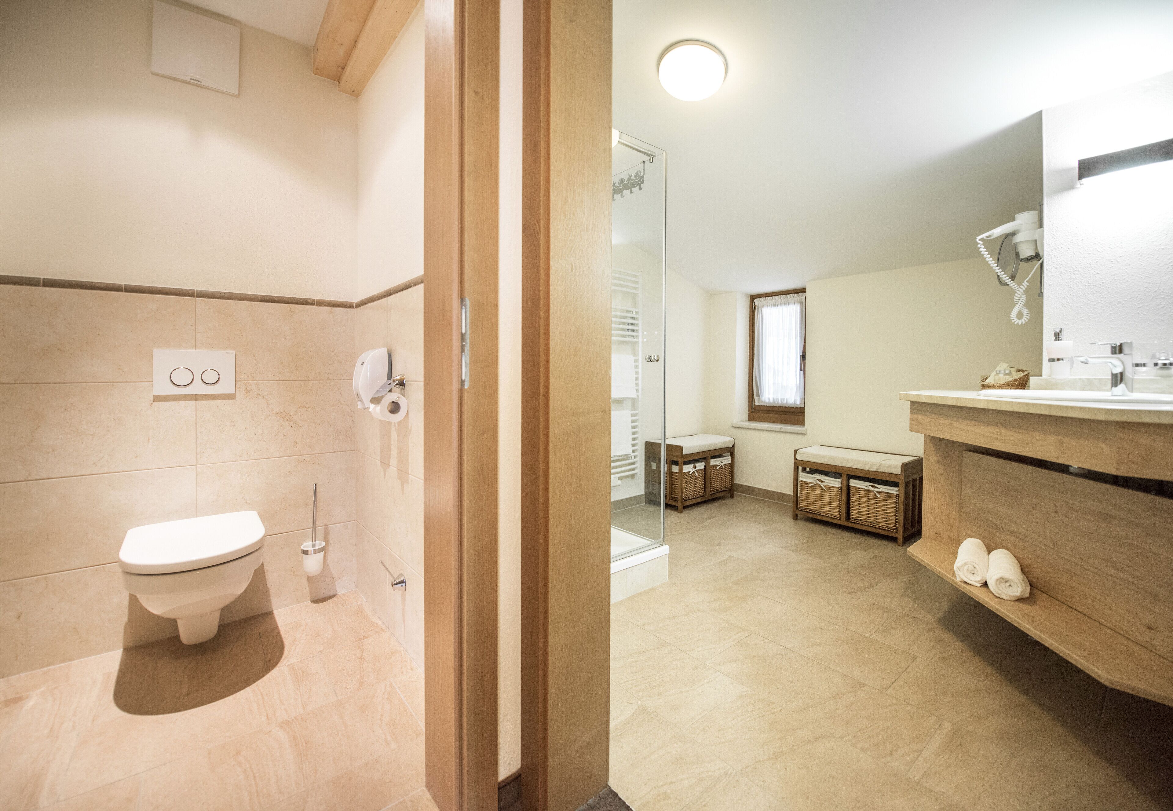 Un baño con inodoro, ducha y lavabo con espejo. Hay cestas y toallas en el suelo.
