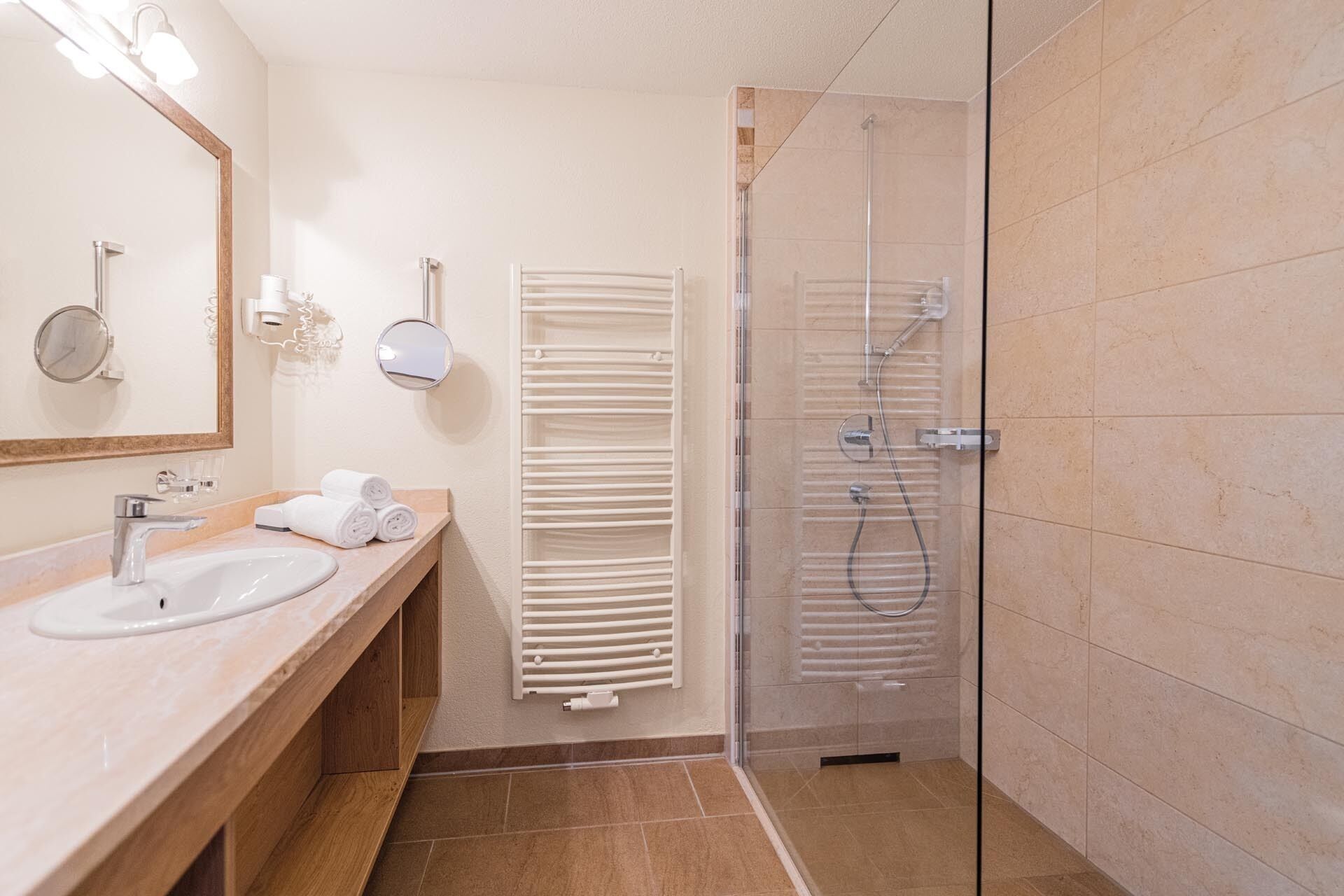 A modern bathroom with a sink, mirror, towel rack, and glass-enclosed shower.