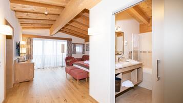 Un'ampia stanza con pavimento in legno, un letto, una scrivania e un bagno con lavandino e specchio.