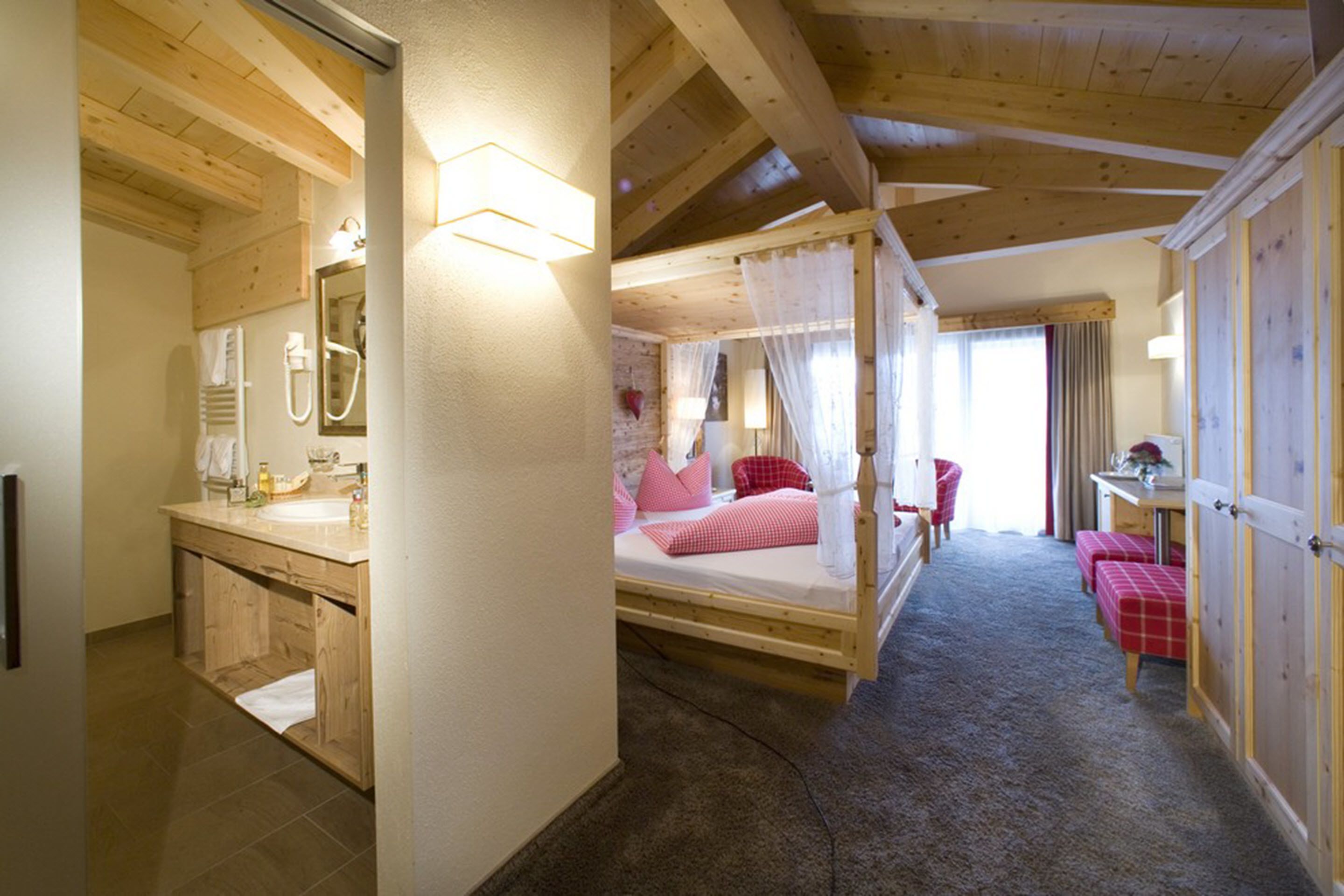 A wooden cabin with a bathroom, a bed with pink bedding, and a red bench.