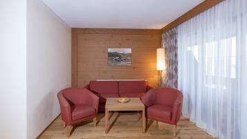 A room with a wooden wall, a red sofa, two red armchairs, a wooden coffee table, and a lamp.