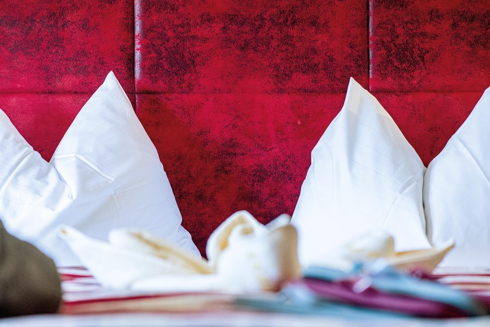 Ein Bett mit weißen Kissen und einer roten Wand mit Struktur im Hintergrund.