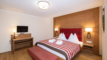 Een hotelkamer met een houten hoofdeinde, een groot bed met rood-witte beddengoed, twee nachtkastjes met lampen, een flatscreen televisie op een houten plank en een bankje voeteneinde van het bed.