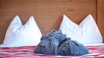 Una cama con colcha a rayas rojas y blancas, dos toallas grises y almohadas blancas frente a un cabecero de madera.
