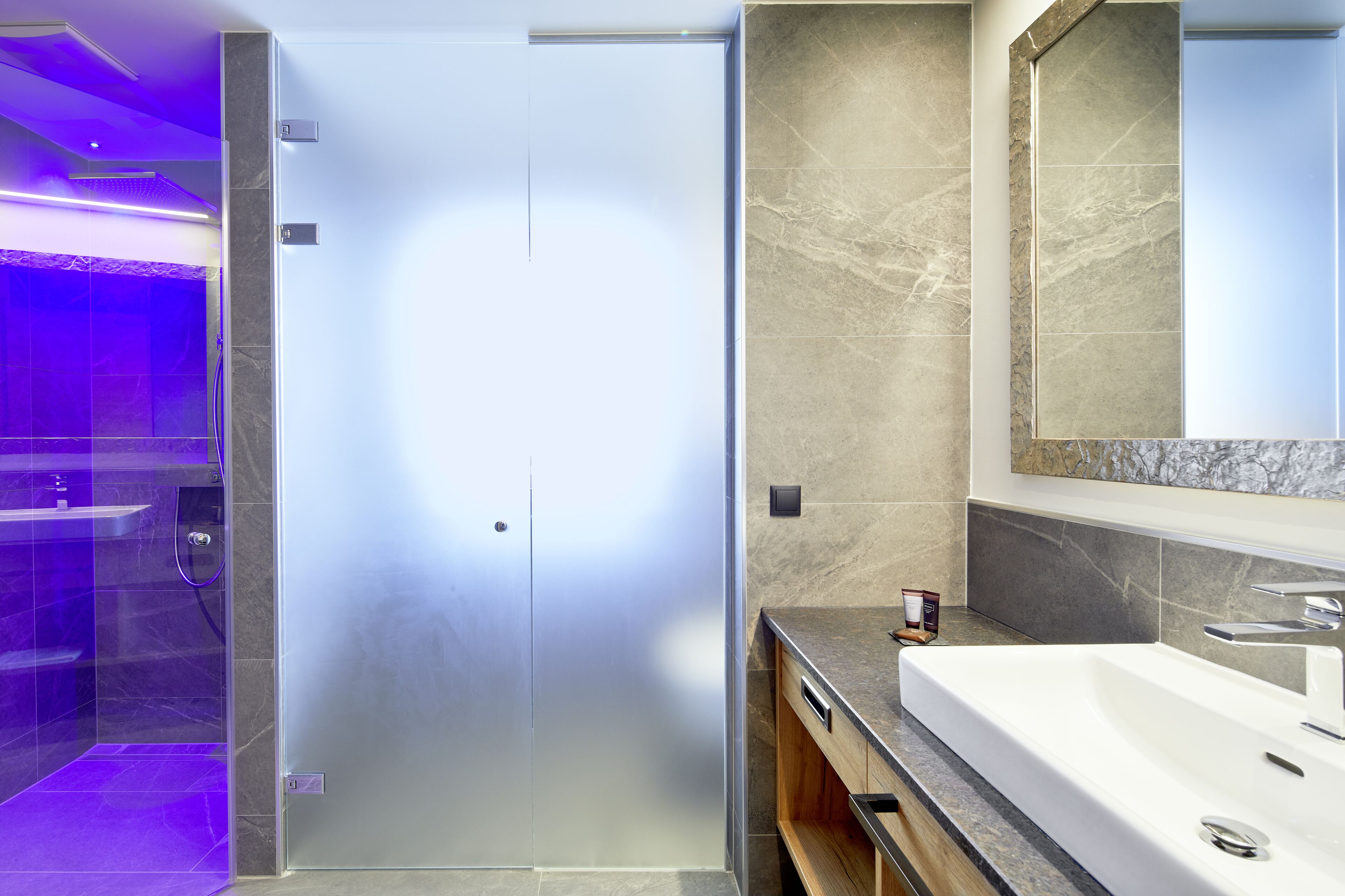Un baño moderno con ducha de vidrio, un lavamanos grande y pared revestida de mármol.