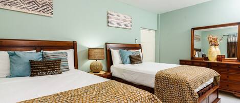 A hotel room with two beds, a wooden headboard, a nightstand with a lamp, a dresser, and a mirror.