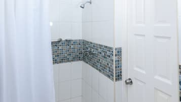 A shower with a white curtain, a tiled wall with a blue mosaic pattern, and a white door with a silver handle.