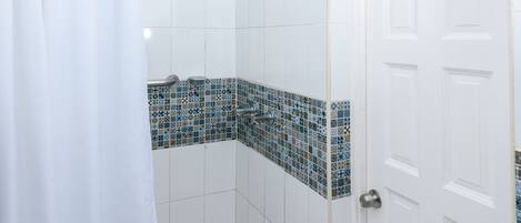 A shower with a white curtain, a tiled wall with a blue mosaic pattern, and a white door with a silver handle.
