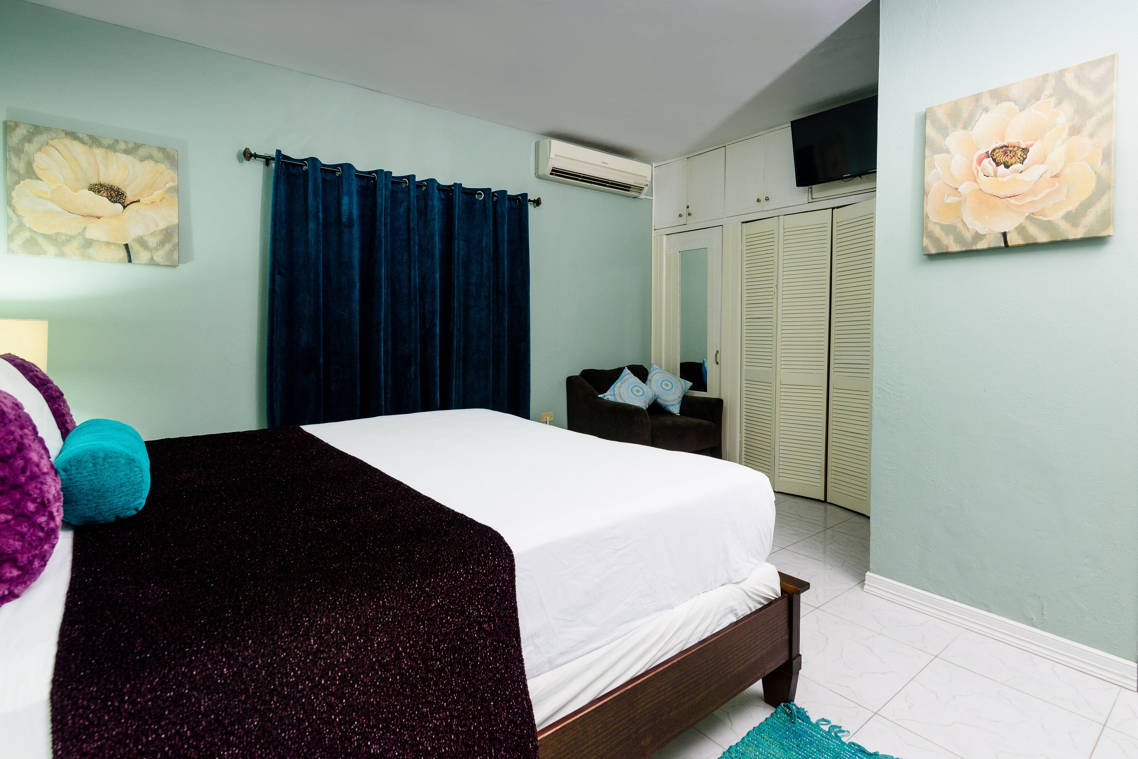 A bedroom with a bed, a dresser, a TV mounted on the wall, and a door with a mirror.