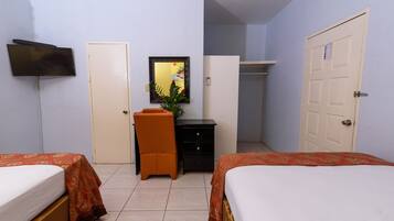 A bedroom with two beds, a desk, a chair, a TV, and a wardrobe.