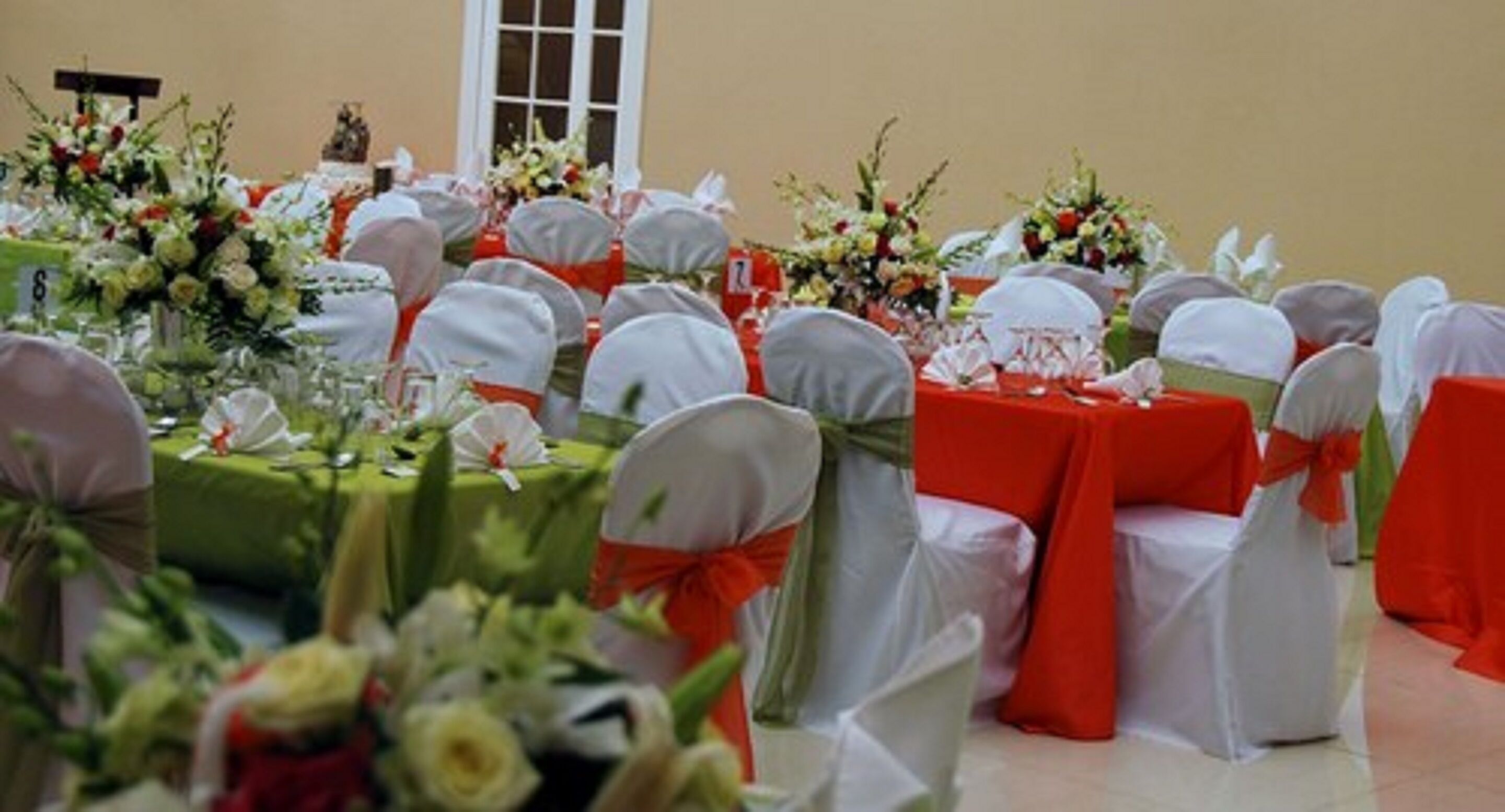 A banquet hall with round tables covered in green tablecloths, white chairs with red sashes, and floral centerpieces.