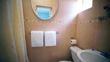 Un baño con dos toallas blancas colgadas en un perchero, un inodoro, un lavamanos y un espejo en la pared.