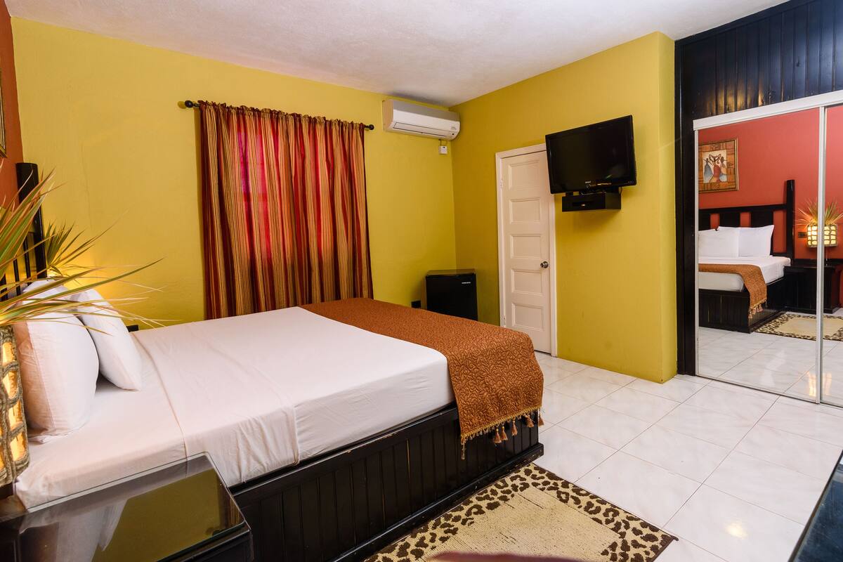 A hotel room with a bed, a television, a mirror, and a door leading to another room.