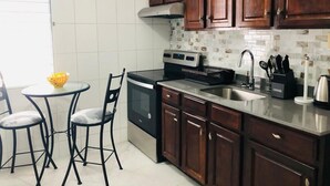 A kitchen with wooden cabinets, a stainless steel sink, a built-in oven, and a small dining area with two chairs and a table. - Hotel Tim Bamboo (Port Antonio)