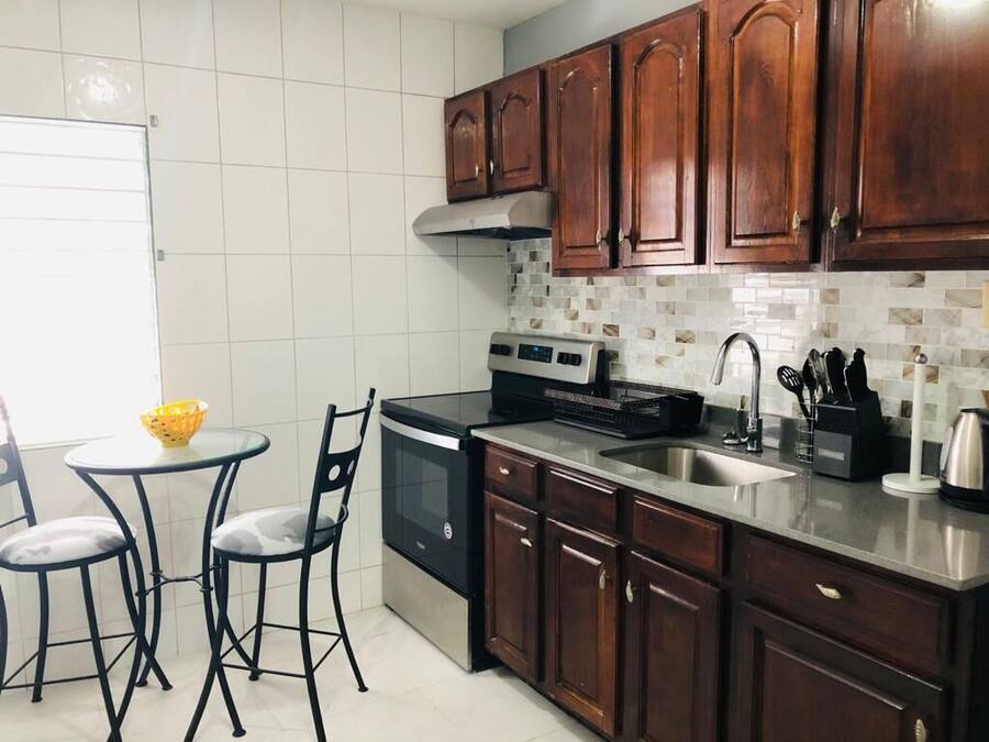 A kitchen with wooden cabinets, a stainless steel sink, a built-in oven, and a small dining area with two chairs and a table.